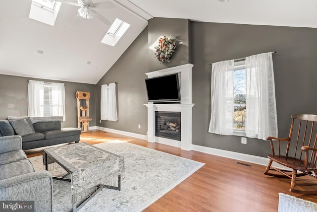 living room featuring light wood-type flooring, a skylight, high vaulted ceiling, and ceiling fan