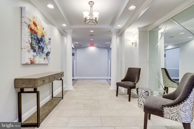 corridor with a tray ceiling, ornate columns, crown molding, and an inviting chandelier