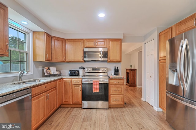 kitchen with light stone countertops, light wood-type flooring, stainless steel appliances, and sink