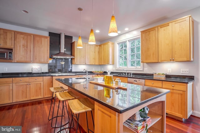 kitchen featuring a kitchen island with sink, wall chimney exhaust hood, dark hardwood / wood-style floors, decorative light fixtures, and stainless steel appliances