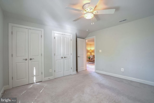 unfurnished bedroom with ceiling fan, light colored carpet, lofted ceiling, and multiple closets