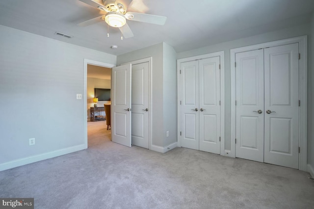 unfurnished bedroom featuring light colored carpet, ceiling fan, and multiple closets