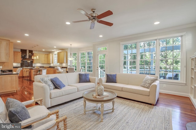 living room featuring ceiling fan, light wood-type flooring, ornamental molding, and a wealth of natural light