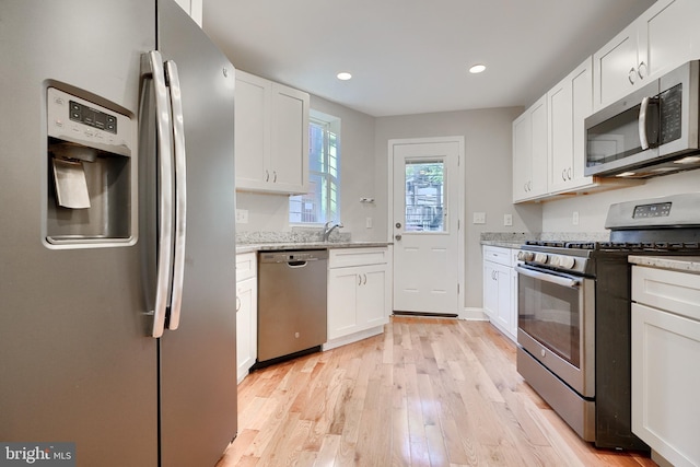 kitchen featuring white cabinets, sink, light stone countertops, light hardwood / wood-style floors, and stainless steel appliances