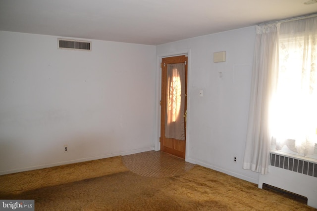 empty room with carpet floors, a healthy amount of sunlight, and radiator heating unit