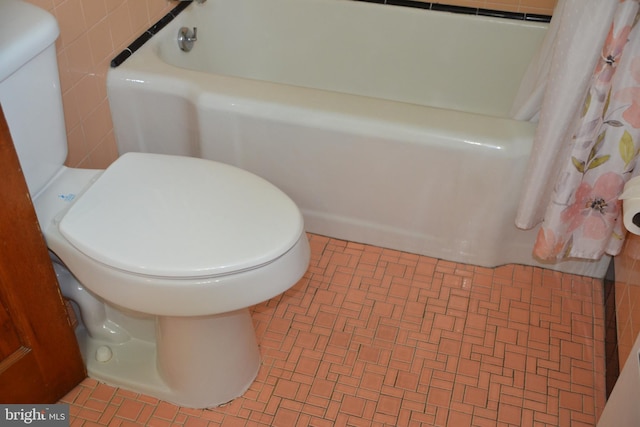 bathroom featuring a tub to relax in, toilet, and tile walls