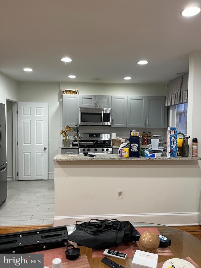 kitchen featuring gray cabinets, light stone counters, and stainless steel appliances