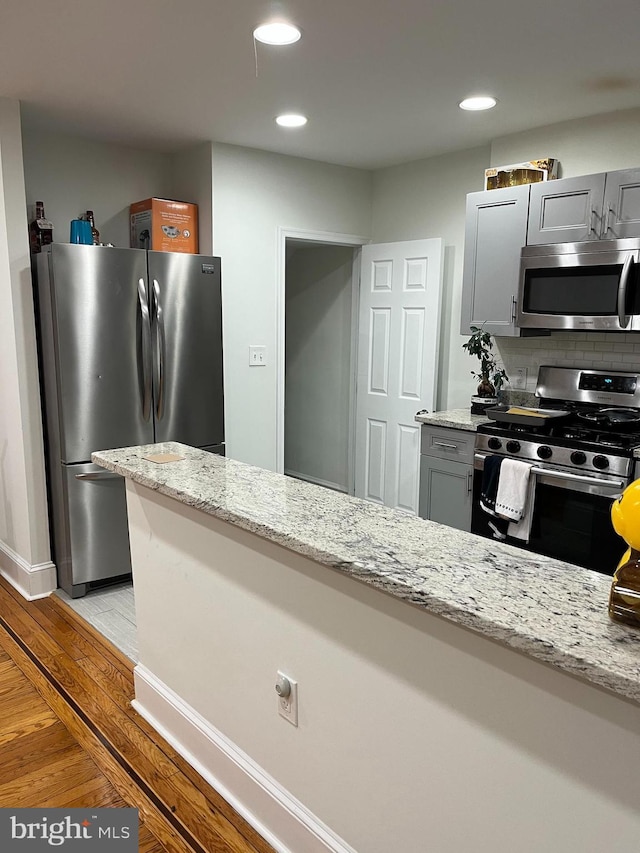 kitchen featuring gray cabinets, light wood-type flooring, light stone countertops, and appliances with stainless steel finishes