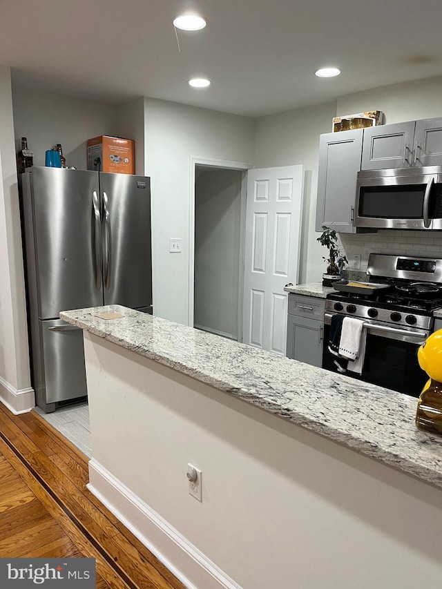 kitchen featuring light stone countertops, light wood-type flooring, stainless steel appliances, and gray cabinets