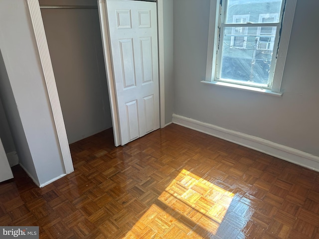 unfurnished bedroom featuring dark parquet flooring and a closet