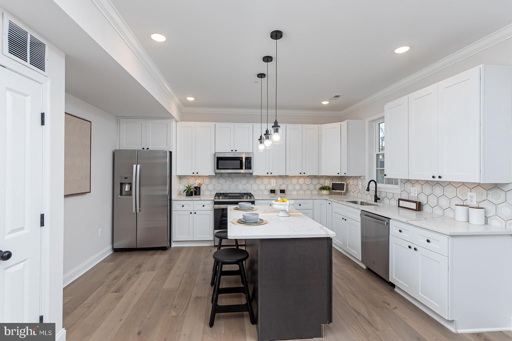 kitchen with stainless steel appliances, a kitchen island, light hardwood / wood-style flooring, decorative light fixtures, and white cabinets