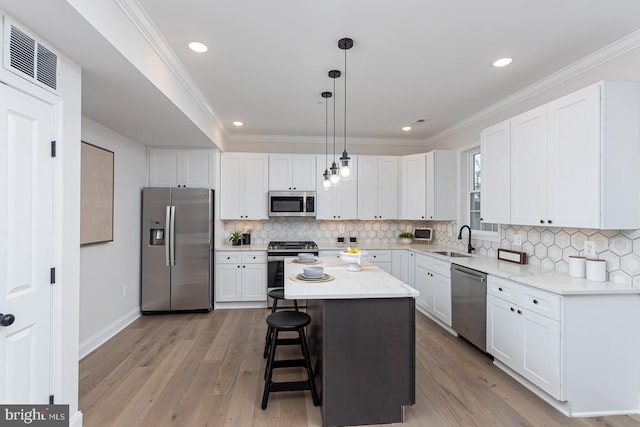 kitchen with stainless steel appliances, a kitchen island, light hardwood / wood-style flooring, decorative light fixtures, and white cabinets