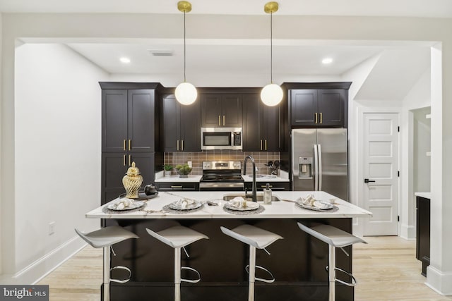 kitchen featuring a kitchen island with sink, hanging light fixtures, stainless steel appliances, and sink