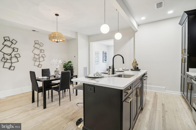 kitchen with decorative light fixtures, light wood-type flooring, a center island with sink, and sink