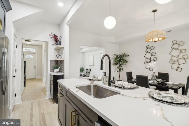 kitchen with light stone counters, sink, decorative light fixtures, and light hardwood / wood-style flooring