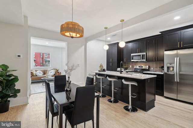 kitchen featuring a breakfast bar, hanging light fixtures, light hardwood / wood-style flooring, an island with sink, and stainless steel appliances