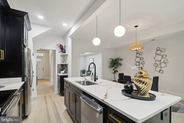 kitchen with appliances with stainless steel finishes, sink, decorative light fixtures, light hardwood / wood-style floors, and an island with sink