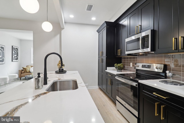 kitchen featuring light wood-type flooring, backsplash, stainless steel appliances, sink, and hanging light fixtures