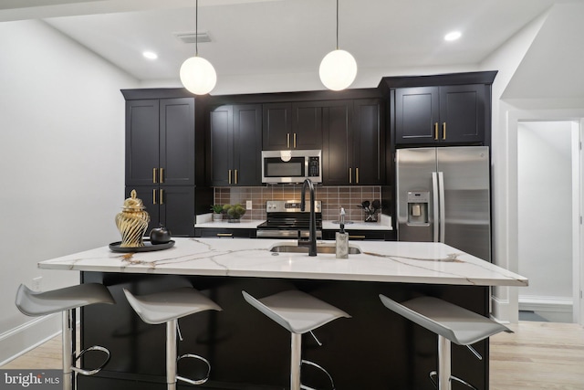 kitchen with backsplash, pendant lighting, stainless steel appliances, and a center island with sink