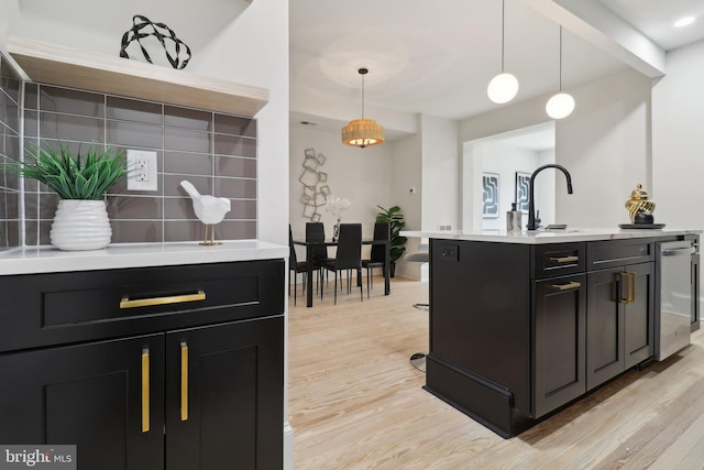 kitchen featuring dishwasher, sink, light hardwood / wood-style flooring, an island with sink, and pendant lighting