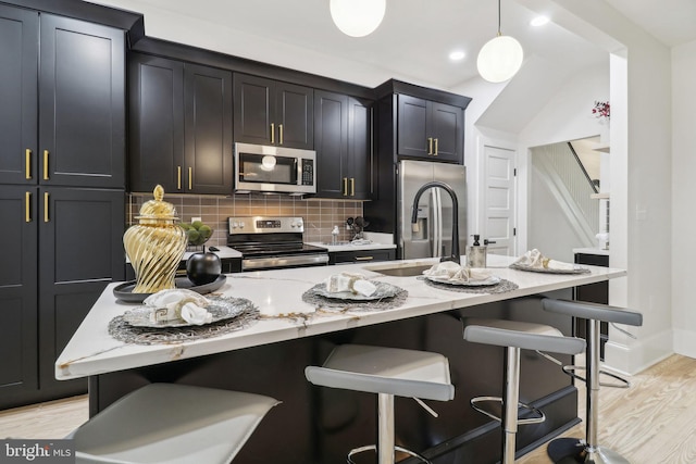 kitchen with stainless steel appliances, pendant lighting, light hardwood / wood-style floors, a kitchen bar, and a center island with sink