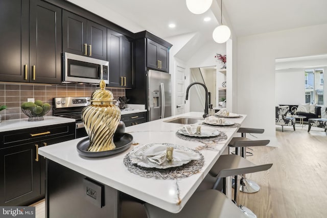 kitchen featuring a center island with sink, hanging light fixtures, decorative backsplash, appliances with stainless steel finishes, and a kitchen bar