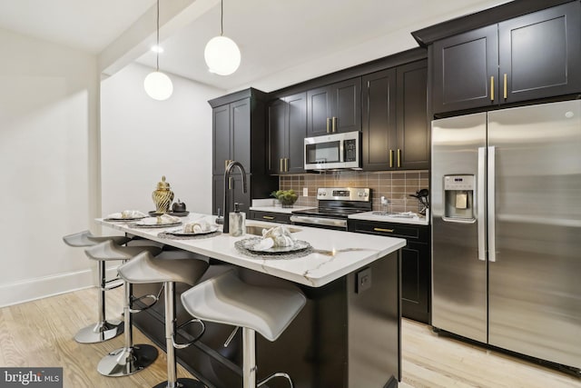 kitchen with a breakfast bar, hanging light fixtures, an island with sink, appliances with stainless steel finishes, and light hardwood / wood-style floors