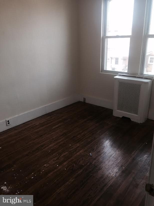 unfurnished room featuring radiator and dark wood-type flooring