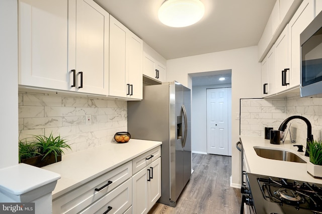 kitchen with white cabinets, sink, appliances with stainless steel finishes, tasteful backsplash, and light hardwood / wood-style floors