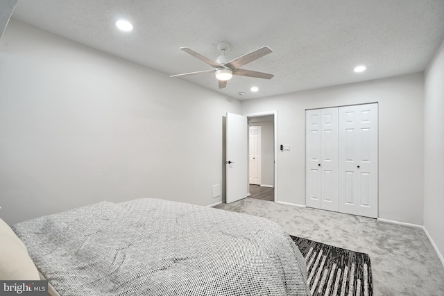 bedroom featuring a textured ceiling, a closet, light colored carpet, and ceiling fan