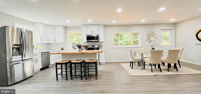 kitchen featuring stainless steel appliances, white cabinetry, light wood-type flooring, and a kitchen breakfast bar