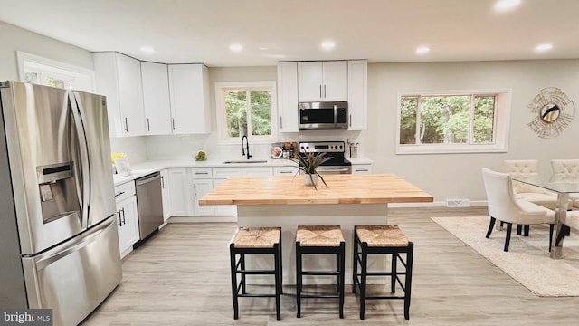 kitchen with a kitchen bar, a kitchen island, white cabinets, appliances with stainless steel finishes, and sink