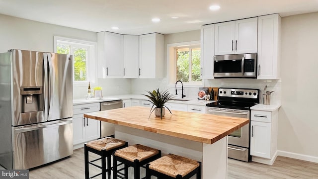 kitchen with appliances with stainless steel finishes, wood counters, a breakfast bar, a kitchen island, and white cabinets