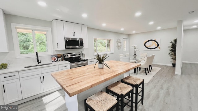 kitchen featuring sink, white cabinets, light wood-type flooring, backsplash, and appliances with stainless steel finishes