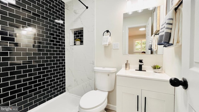 bathroom featuring toilet, tiled shower, and vanity