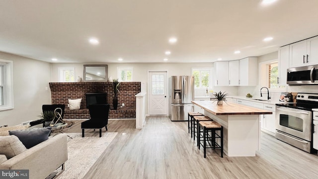 kitchen with stainless steel appliances, a kitchen island, butcher block countertops, a breakfast bar area, and white cabinetry