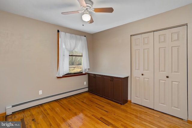 unfurnished bedroom with ceiling fan, a closet, light wood-type flooring, and a baseboard heating unit