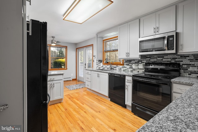 kitchen with light stone countertops, light wood-type flooring, ceiling fan, sink, and black appliances