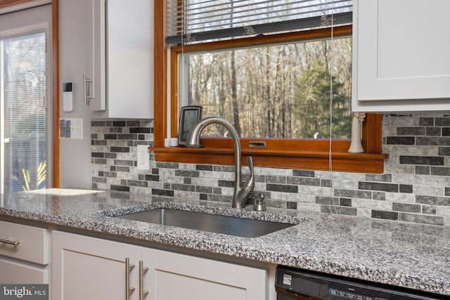 kitchen with white cabinets, decorative backsplash, black dishwasher, and sink