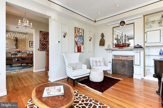 sitting room featuring a brick fireplace, wood-type flooring, and an inviting chandelier