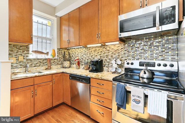 kitchen with appliances with stainless steel finishes, backsplash, light stone counters, and sink