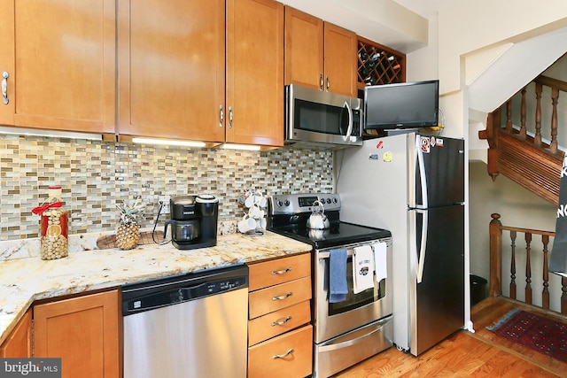 kitchen with backsplash, light stone counters, stainless steel appliances, and light hardwood / wood-style floors