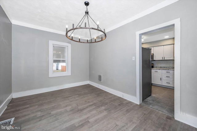unfurnished dining area with dark hardwood / wood-style floors, crown molding, and a chandelier
