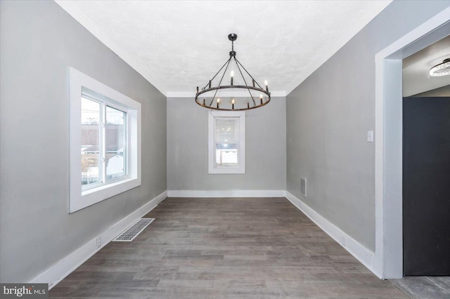 unfurnished dining area with hardwood / wood-style flooring, a textured ceiling, and an inviting chandelier