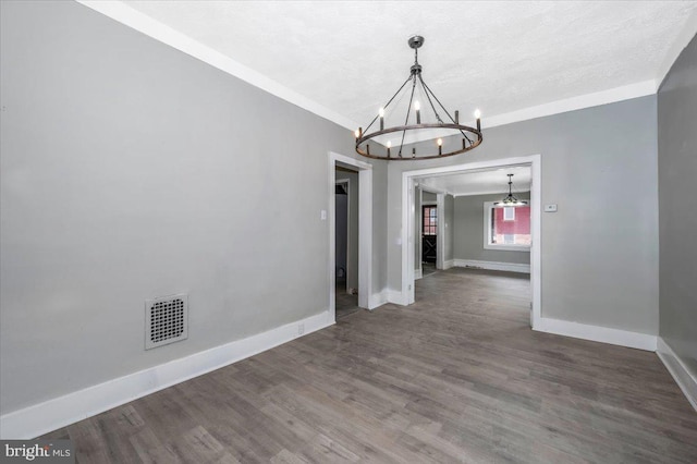 unfurnished dining area featuring dark hardwood / wood-style floors, ornamental molding, a textured ceiling, and a chandelier