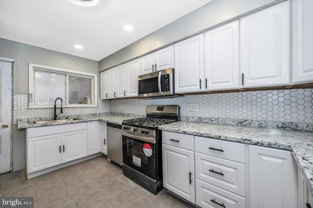 kitchen with light stone countertops, white cabinetry, sink, stainless steel appliances, and decorative backsplash