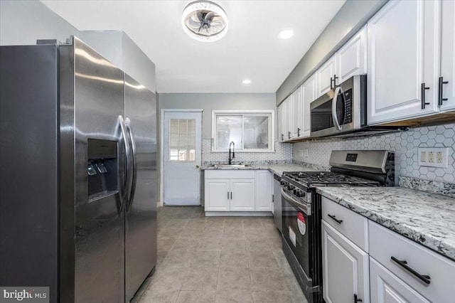 kitchen with light stone countertops, white cabinetry, sink, stainless steel appliances, and tasteful backsplash