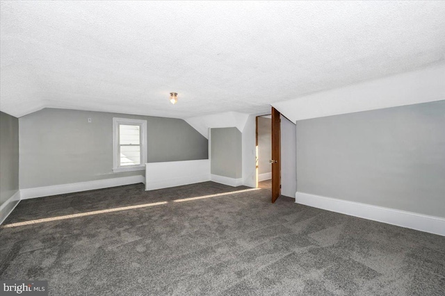 additional living space with dark carpet, a textured ceiling, and vaulted ceiling