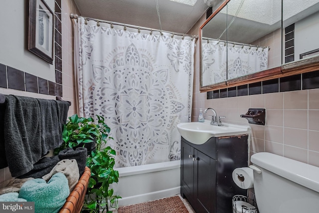 bathroom with a textured ceiling, vanity, toilet, and tile walls