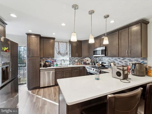 kitchen featuring kitchen peninsula, light wood-type flooring, dark brown cabinetry, stainless steel appliances, and decorative light fixtures